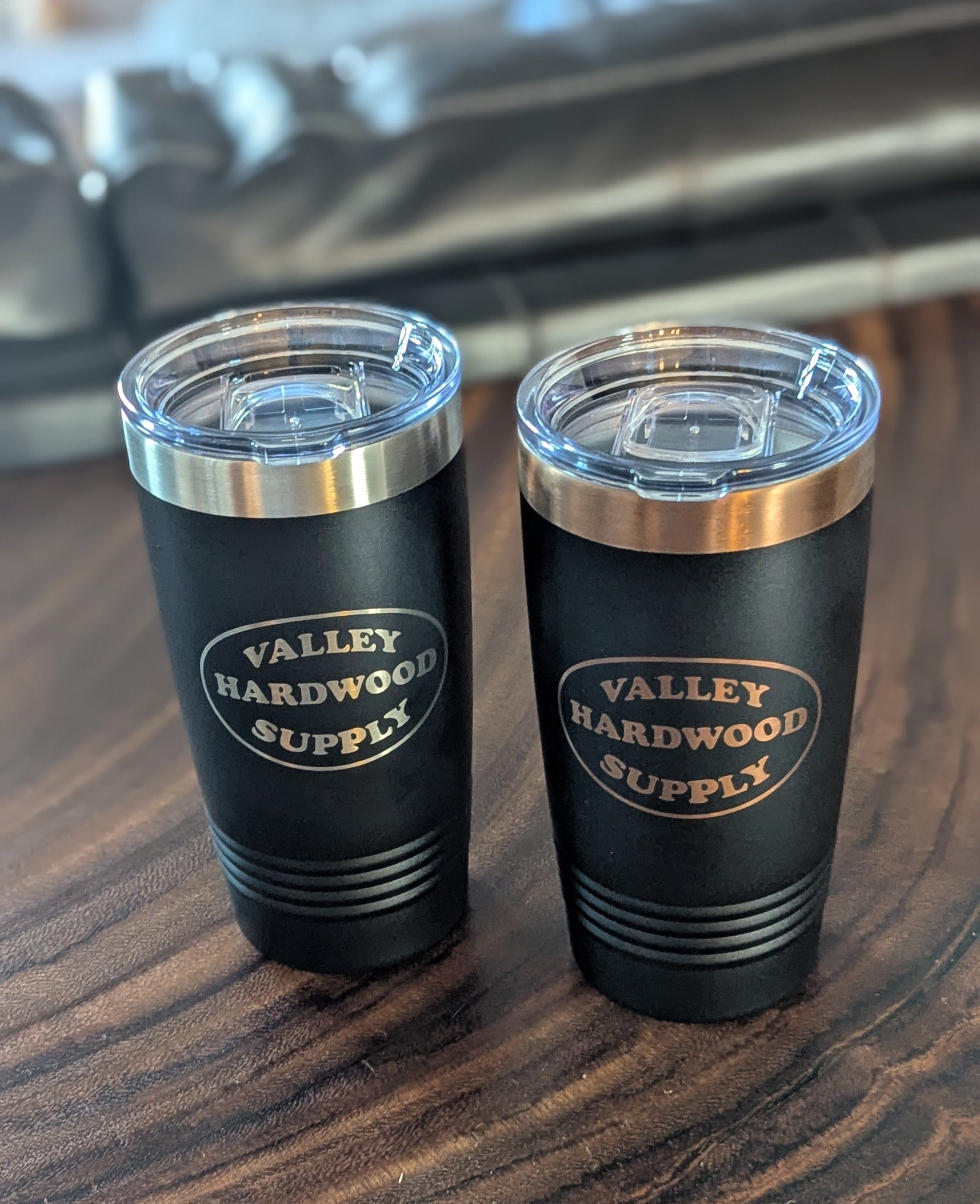 Two black tumblers with silver lids on a wooden surface, branded 'Valley Hardwood Supply'.